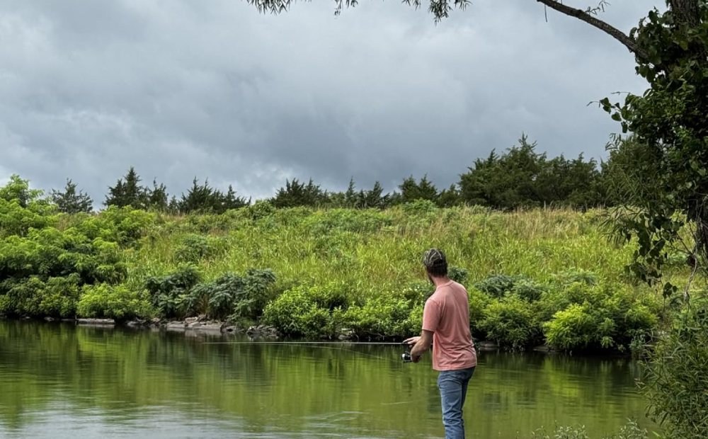 An angler casting a spinning reel from the rocks on a quiet pond